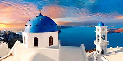 A pink tinged sunset over blue domed buildings in Santorini, Greece.